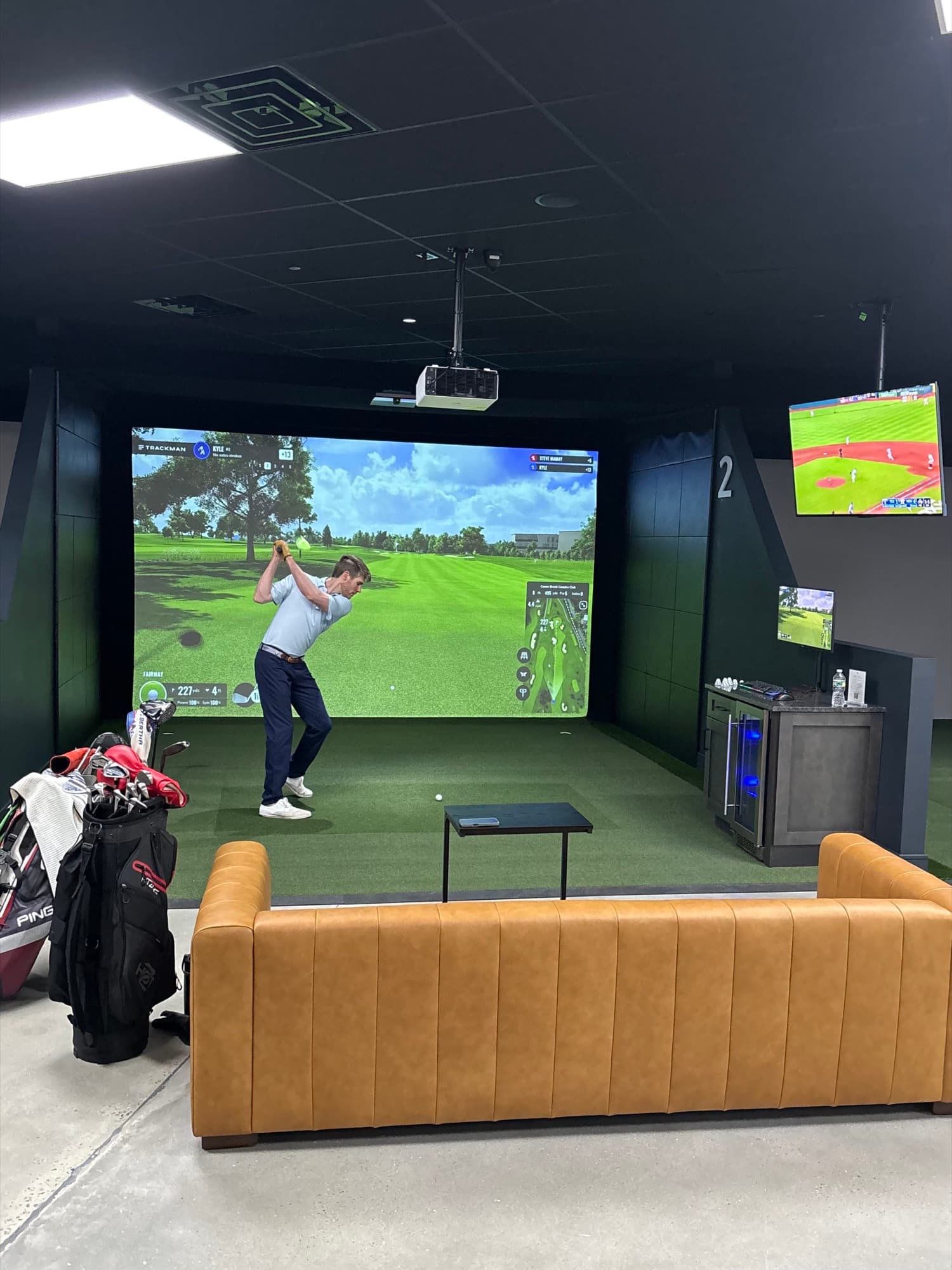 A golfer mid-swing in a Trackman simulator bay at Unbound Golf