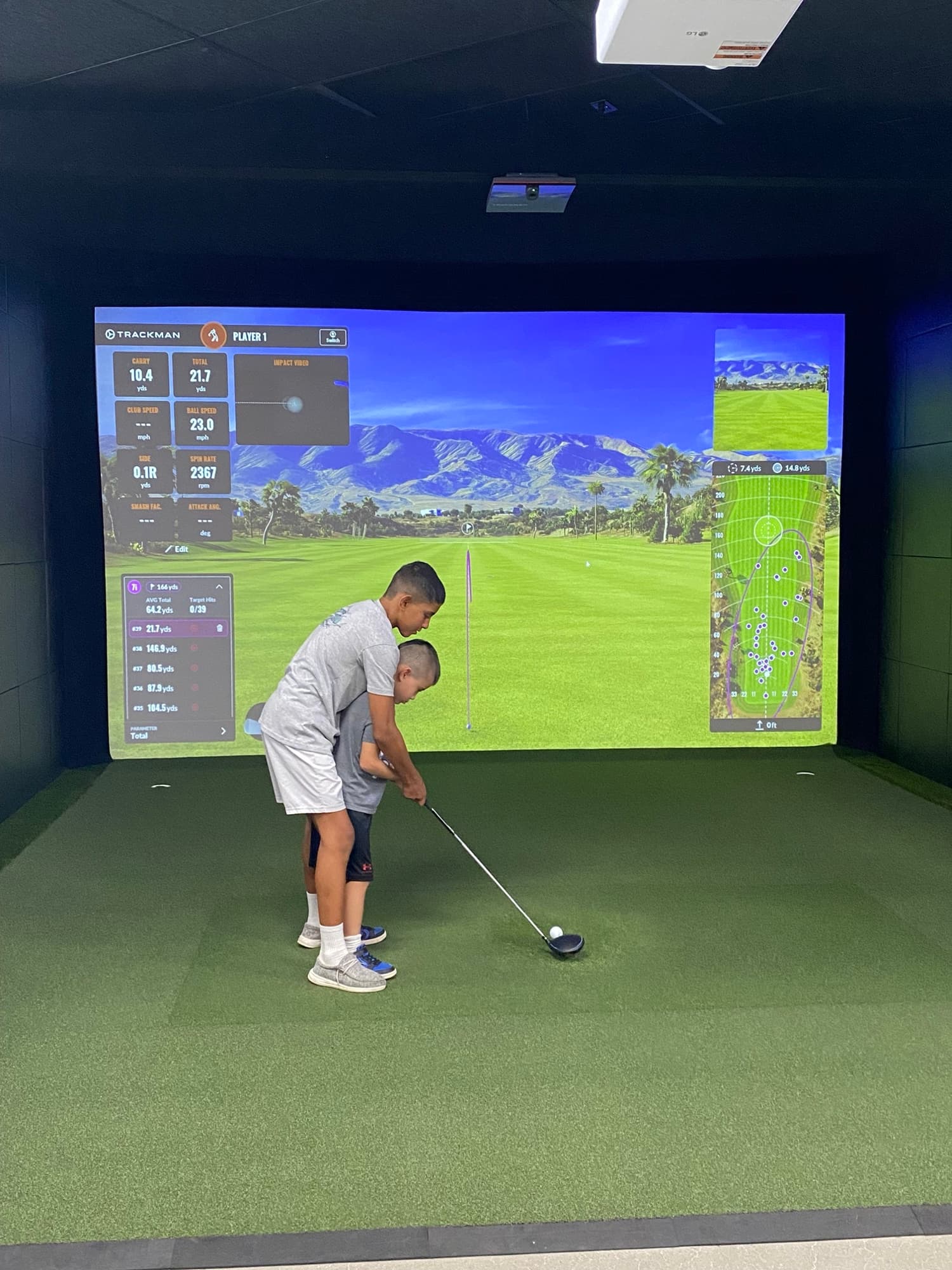 Two kids practicing together in a simulator bay at Unbound Golf