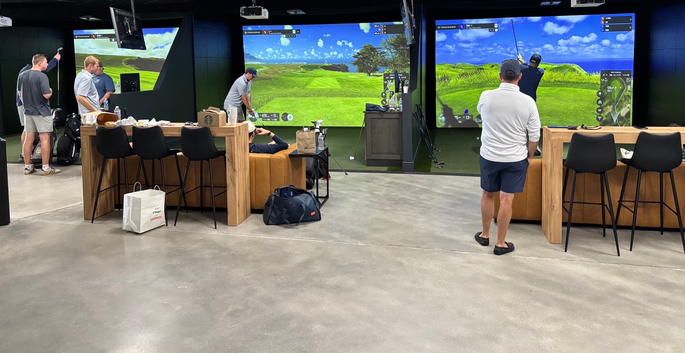 Golfers playing across Trackman simulator bays at Unbound Golf